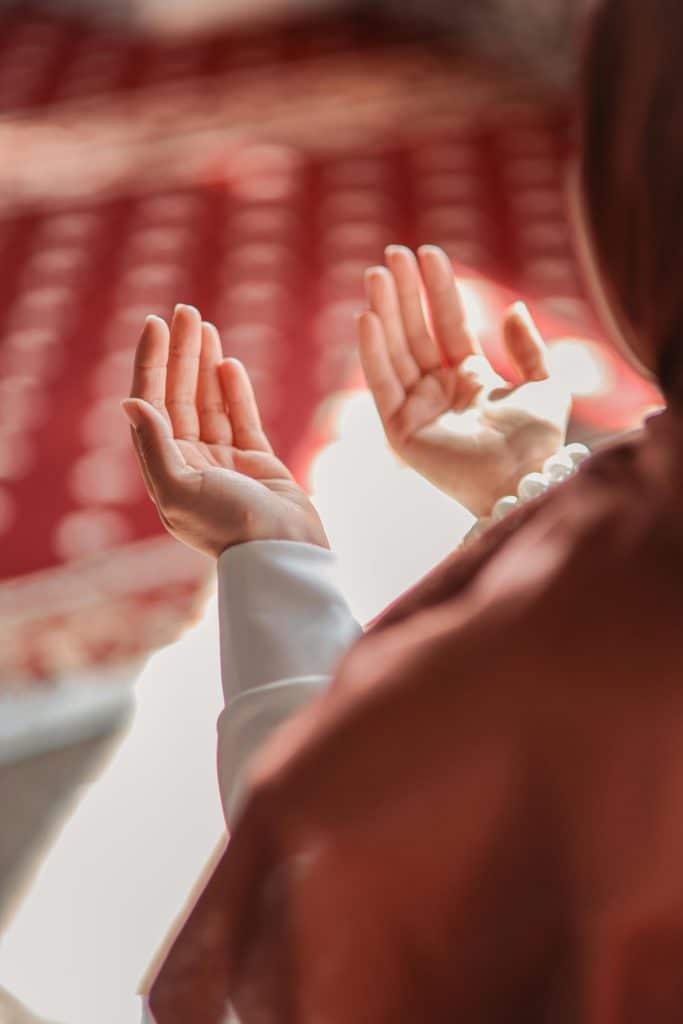 Muslim woman praying in a mosque, hands raised in devotion, emphasizing spirituality and faith.